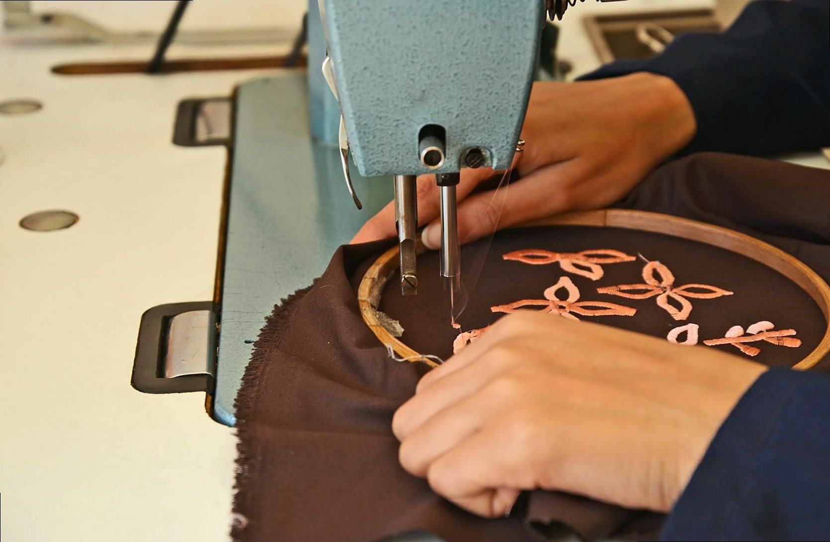 Gros plan de mains brodant du tissu à la machine dans un atelier artisanal de Fès.