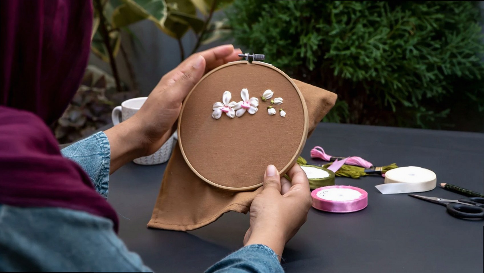 Gros plan de mains travaillant sur une broderie florale en extérieur.